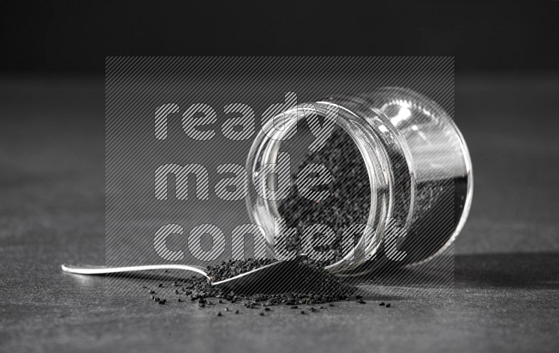 A glass jar full of black seeds flipped and seeds spreaded out with a metal spoon full of the seeds on a black flooring in different angles