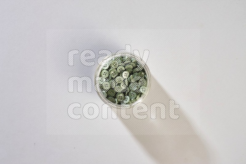 A glass jar full of colored buttons on grey background