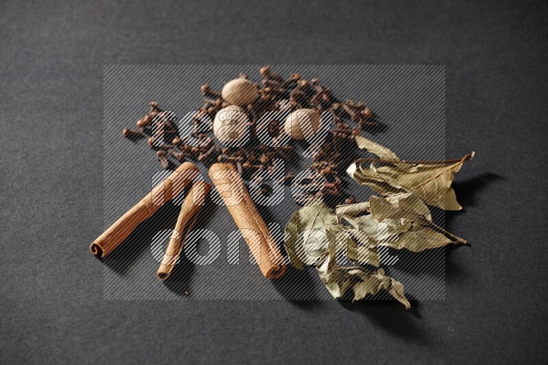 Cloves, ginger, bay laurel and cinnamon sticks on black flooring