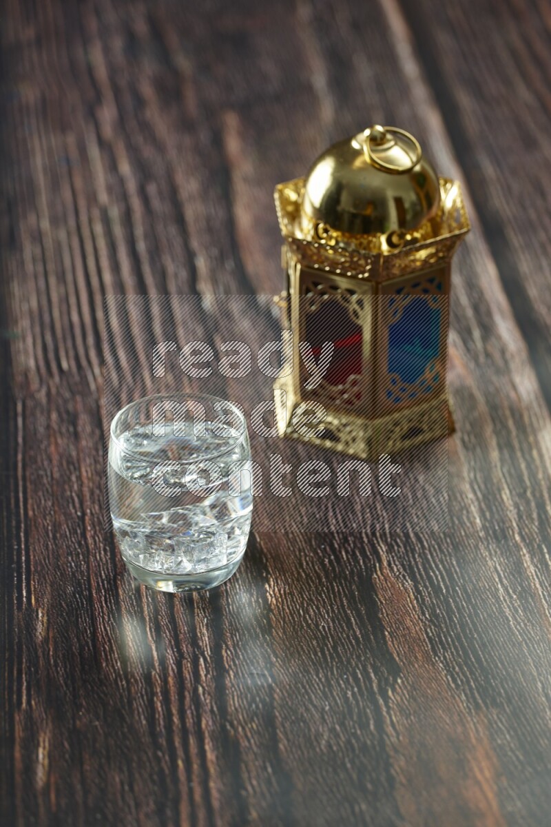 A golden lantern with different drinks, dates, nuts, prayer beads and quran on brown wooden background
