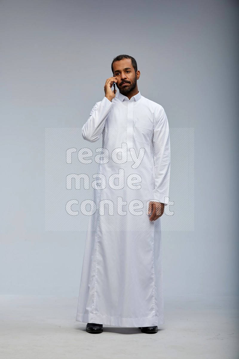 Saudi man wearing Thob standing talking on phone on Gray background