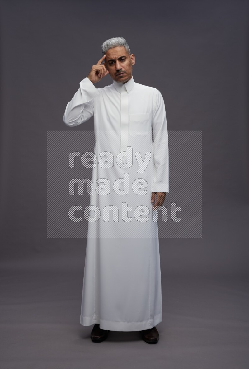 Saudi man wearing thob standing interacting with the camera on gray background