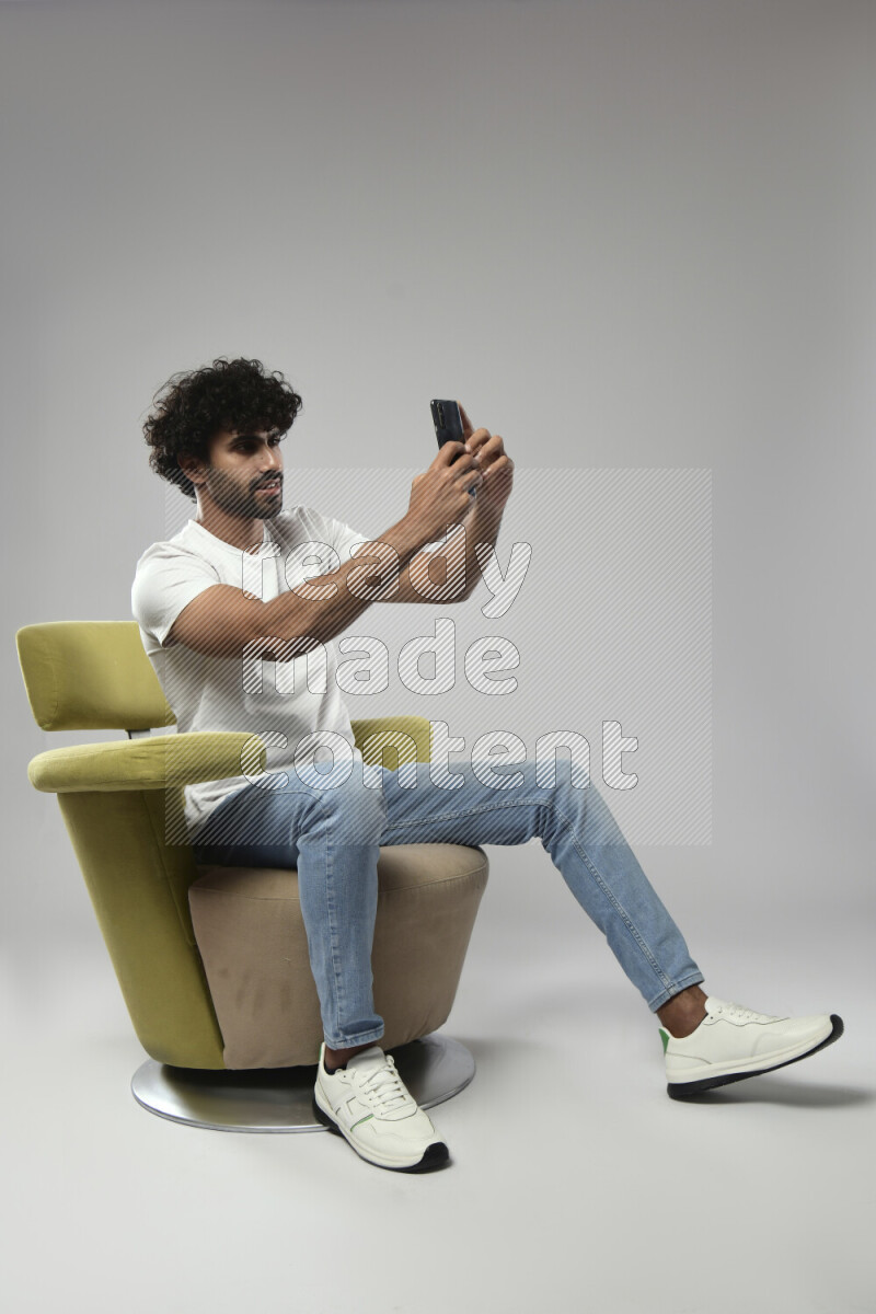 A man wearing casual sitting on a chair taking a selfie on white background
