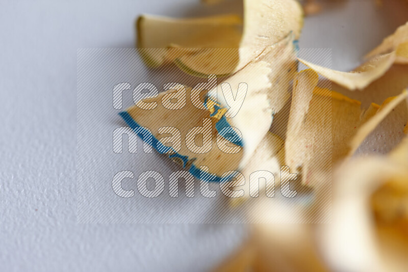A close-up showing a small pile of pencil shavings with varied color edges on grey background