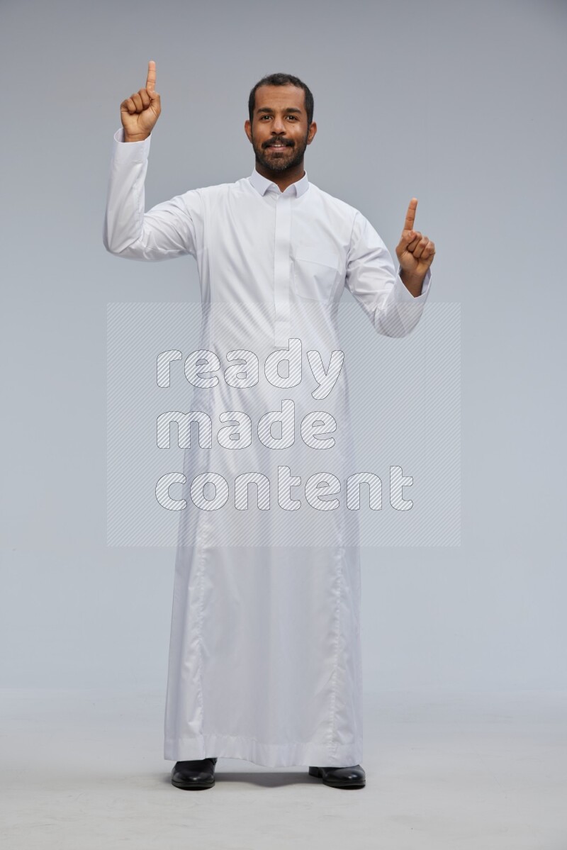 Saudi man Wearing Thob standing interacting with the camera on Gray background
