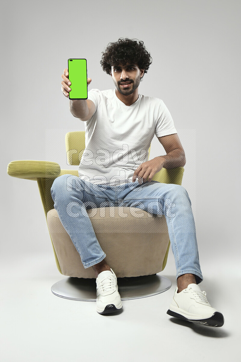 رجل يرتدي ملابس كاجوال يجلس علي كرسي و يحمل هاتف علي خلفية بيضاء