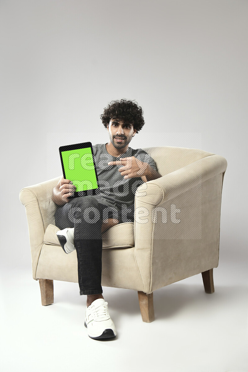رجل يرتدي ملابس كاجوال يجلس علي كرسي و يحمل تابلت علي خلفية بيضاء