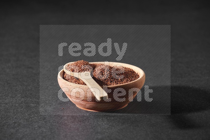 A wooden bowl full of garden cress seeds and a wooden spoon full of the seeds on it on a black flooring