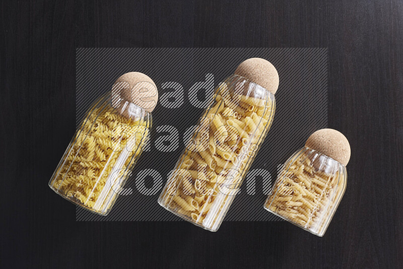 Raw pasta in glass jars on black background