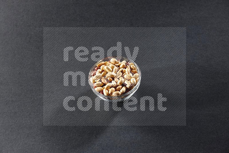 A glass bowl full of peeled peanuts on a black background in different angles