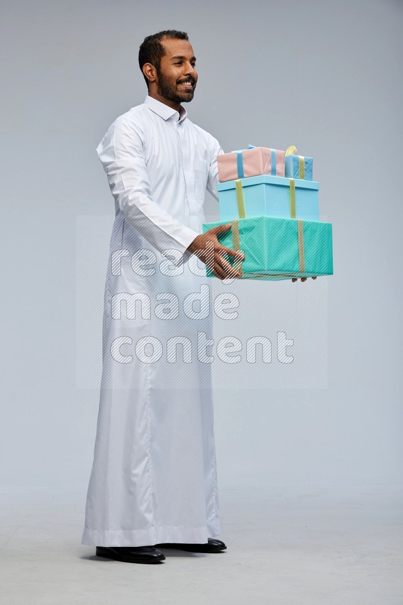 Saudi man Wearing thob standing holding gift box on Gray background
