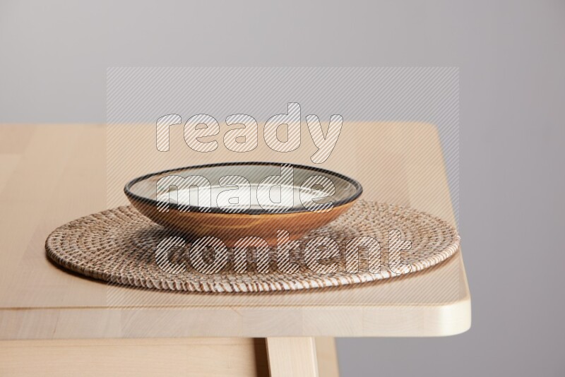multi-colored pottery Plate placed on a big light colored straw placemat on the edge of wooden table