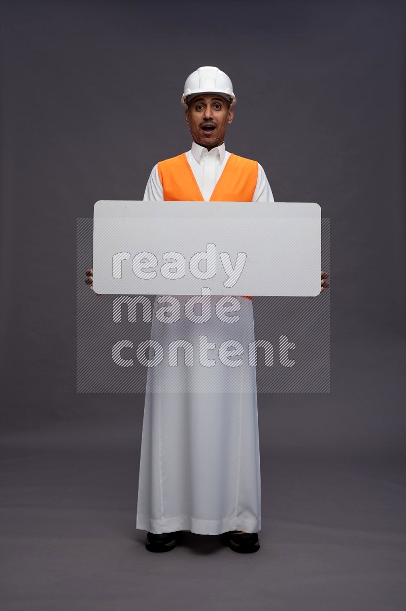 Saudi man wearing thob with engineer vest standing holding board on gray background
