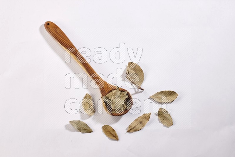 A wooden ladle filled with dried bay leaves on white flooring in different angles