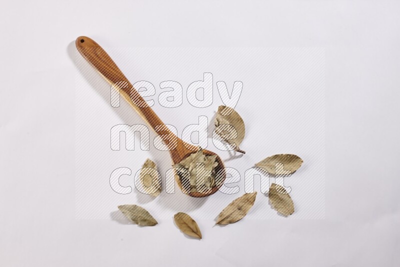 A wooden ladle filled with dried bay leaves on white flooring in different angles