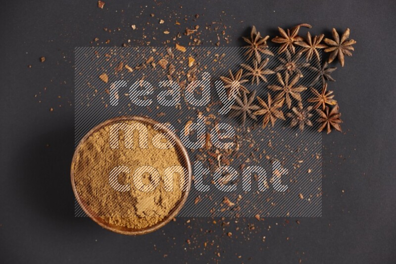 Star Anise powder in a wooden bowl with star anise beside it on a black background