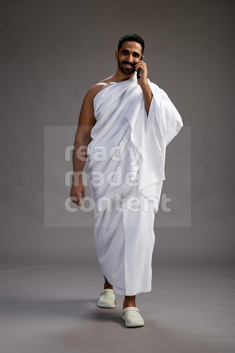 A man wearing Ehram Standing talking on phone on gray background