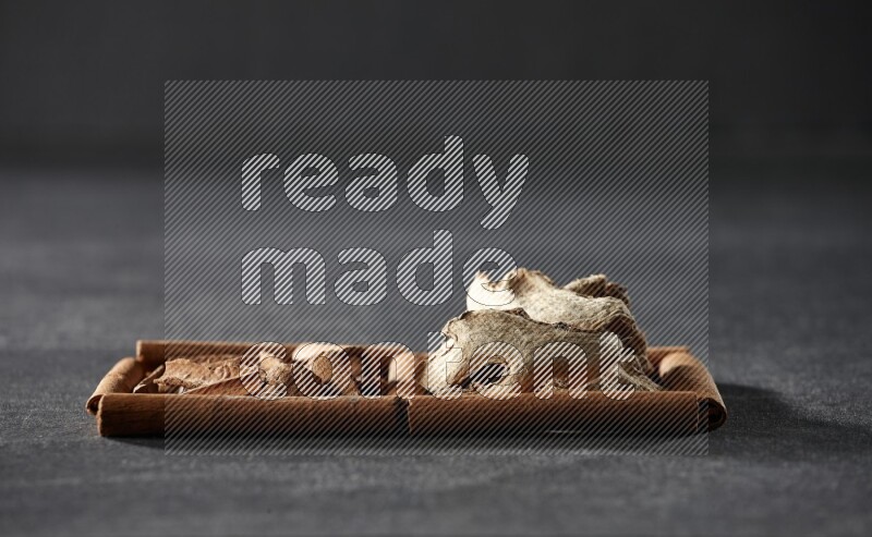 مربعان من أعواد القرفة ممتلئان بقطع من القرفة والزنجبيل المجفف علي خلفية سوداء