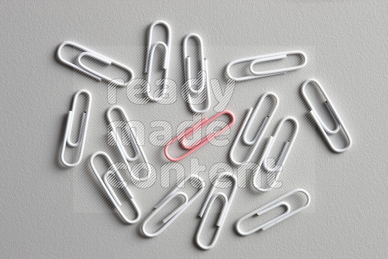 A bunch of white paper clips with a different colored paper clip in the center on grey background
