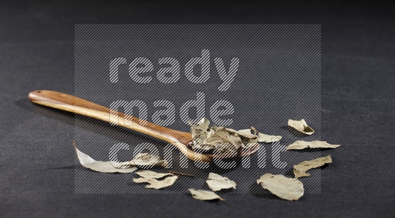 A wooden ladle filled with dried bay leaves on black flooring