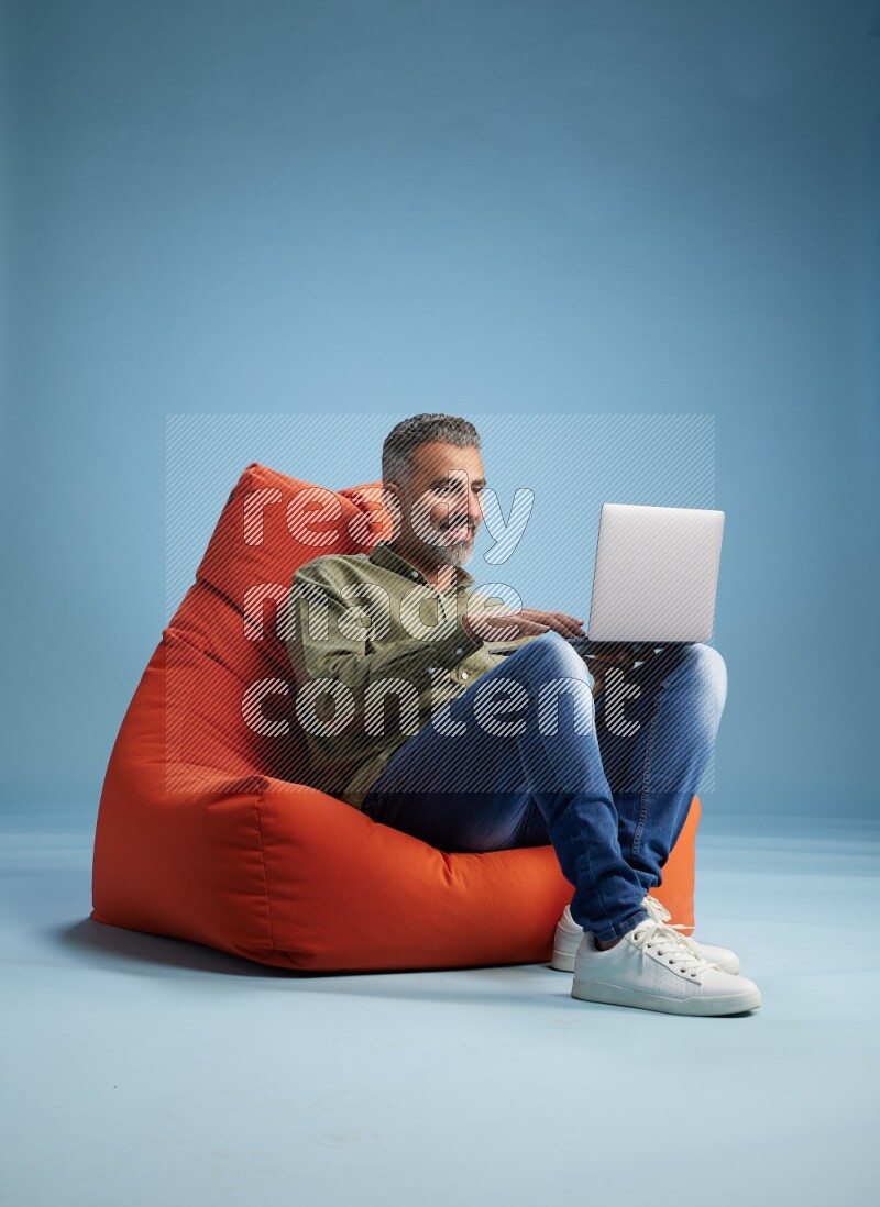 A man sitting on an orange beanbag and working on laptop