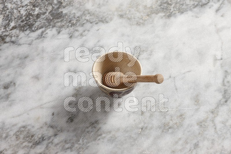 Decorative Pottery Bowl with wooden honey handle in it, on grey marble flooring, 65 degree angle