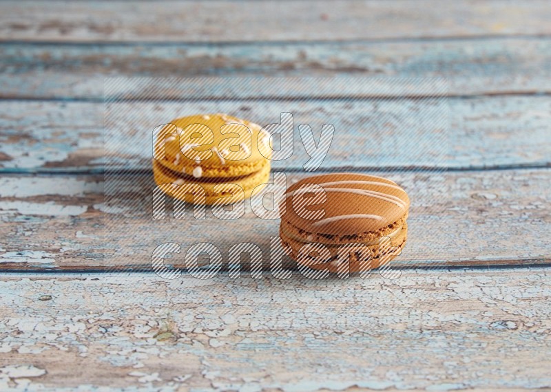 45º Shot of of two assorted Brown Irish Cream, and Yellow Piña Colada macarons on light blue background