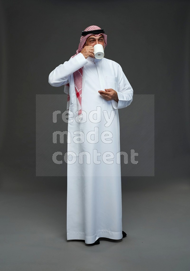 Saudi man with shomag Standing holding mug on gray background