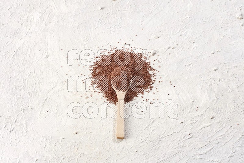 A wooden spoon full of garden cress seeds on a textured white flooring
