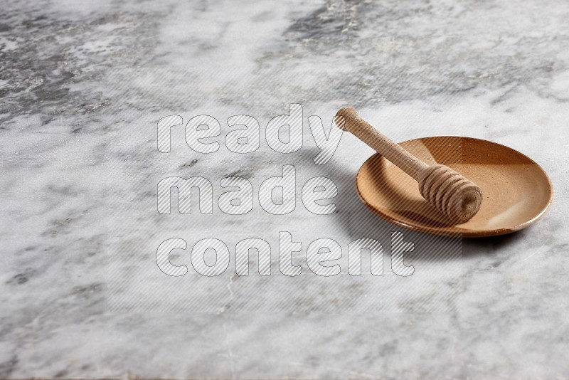 Multicolored Pottery Plate with wooden honey handle in it, on grey marble flooring, 45 degree angle