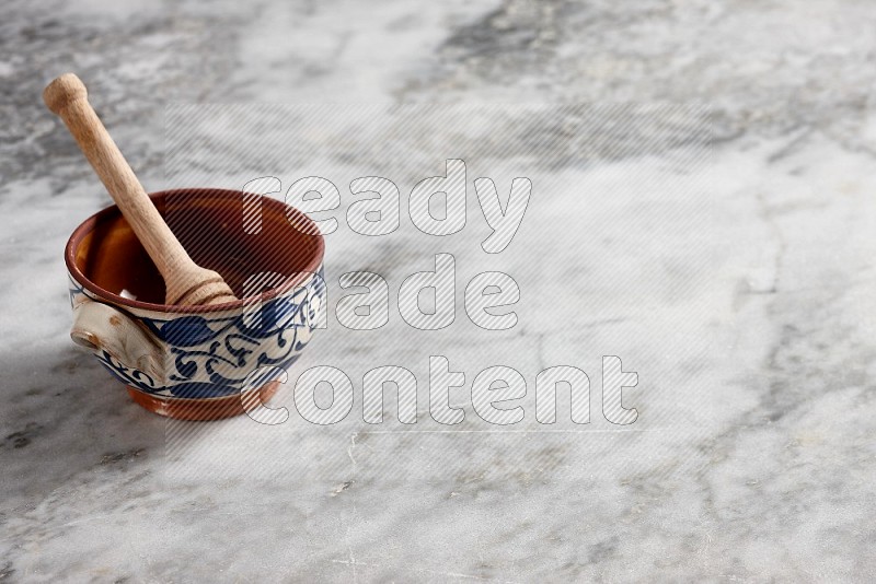 Decorative Pottery Pot with wooden honey handle in it, on grey marble flooring, 45 degree angle