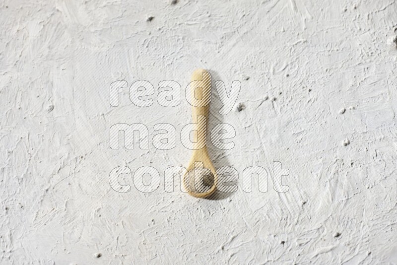 A wooden spoon full of white pepper powder on textured white flooring