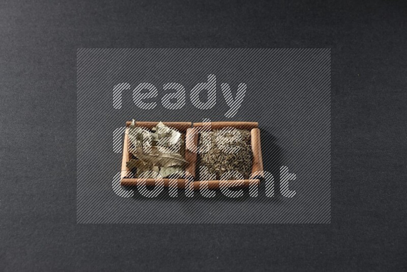 مربعان من أعواد القرفة ممتلئان بحبوب الكمون وأوراق الغار علي خلفية سوداء