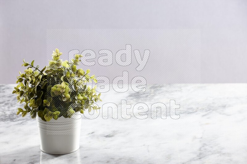 Green artificial plant in white pot on light grey marble background