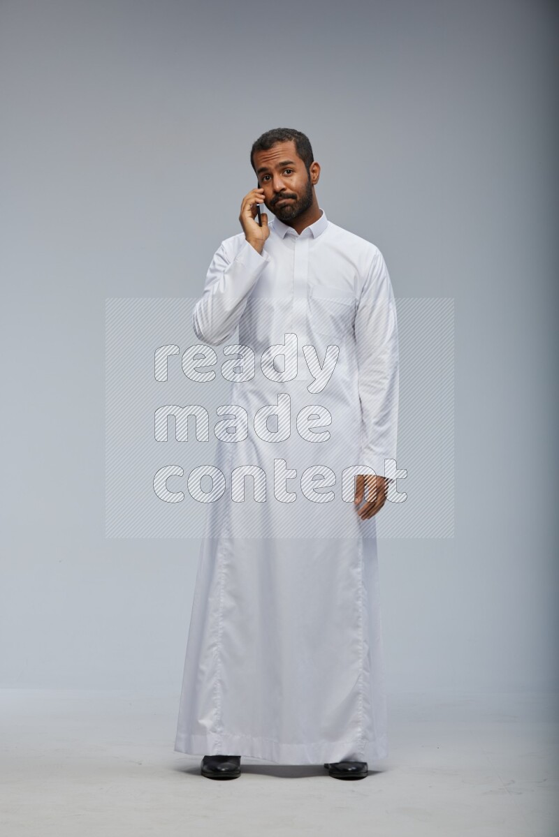 Saudi man wearing Thob standing talking on phone on Gray background