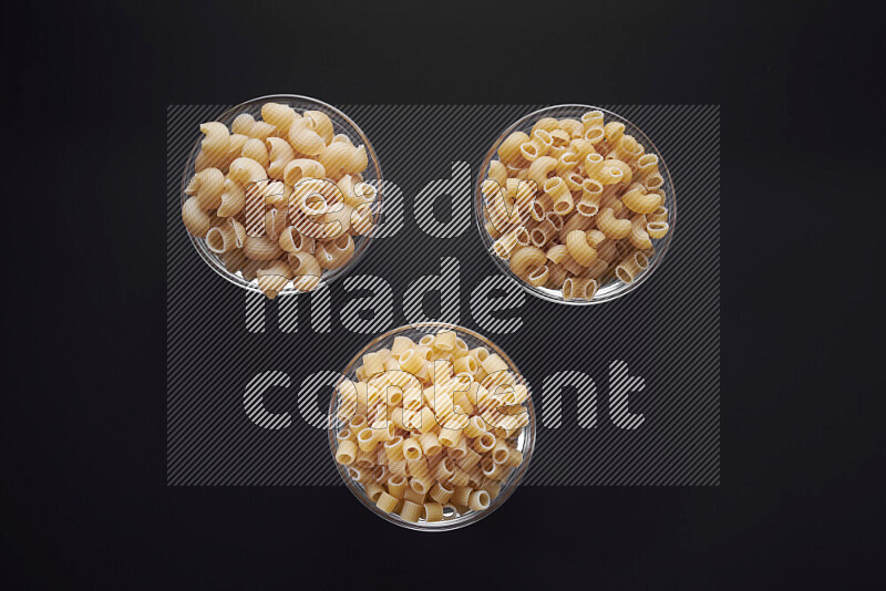 Different pasta types in glass bowls on black background