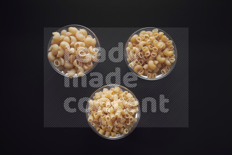 Different pasta types in glass bowls on black background