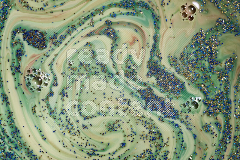 A close-up of sparkling blue and gold glitter scattered on swirling green and red background