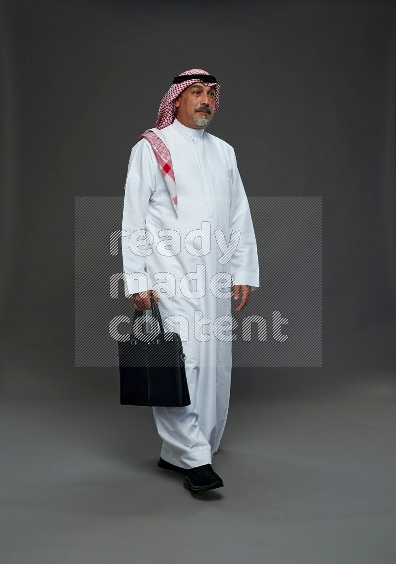 Saudi man with shomag Standing holding bag on gray background