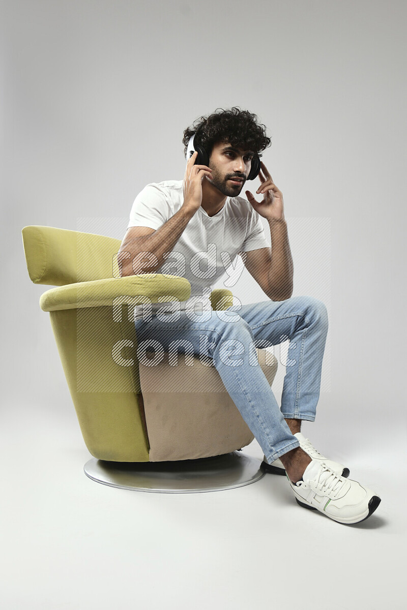 A man wearing casual sitting on a chair putting on headphones on white background