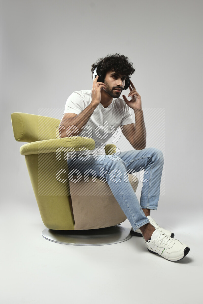 A man wearing casual sitting on a chair putting on headphones on white background