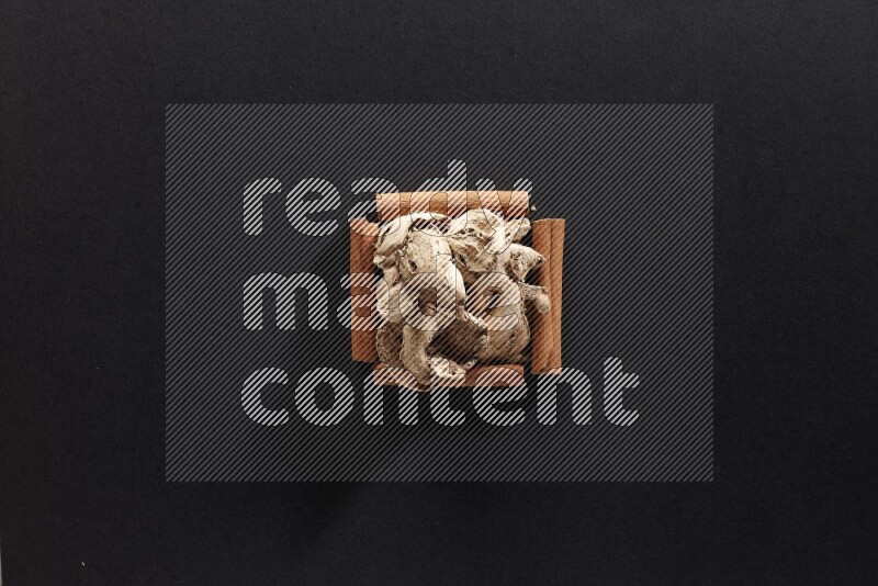 أربعة من أعواد القرفة مكونة شكل مربع بداخلها زنجبيل مجفف علي خلفية سوداء