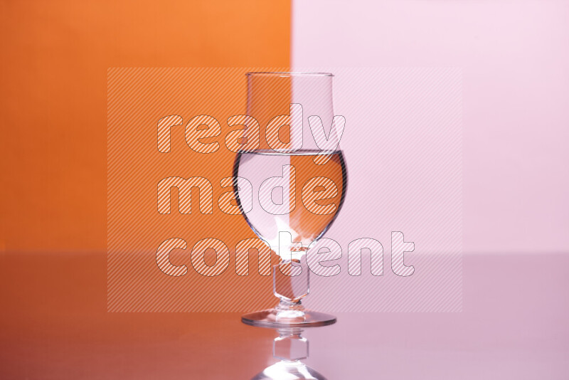 The image features a clear glassware filled with water, set against orange and rose background