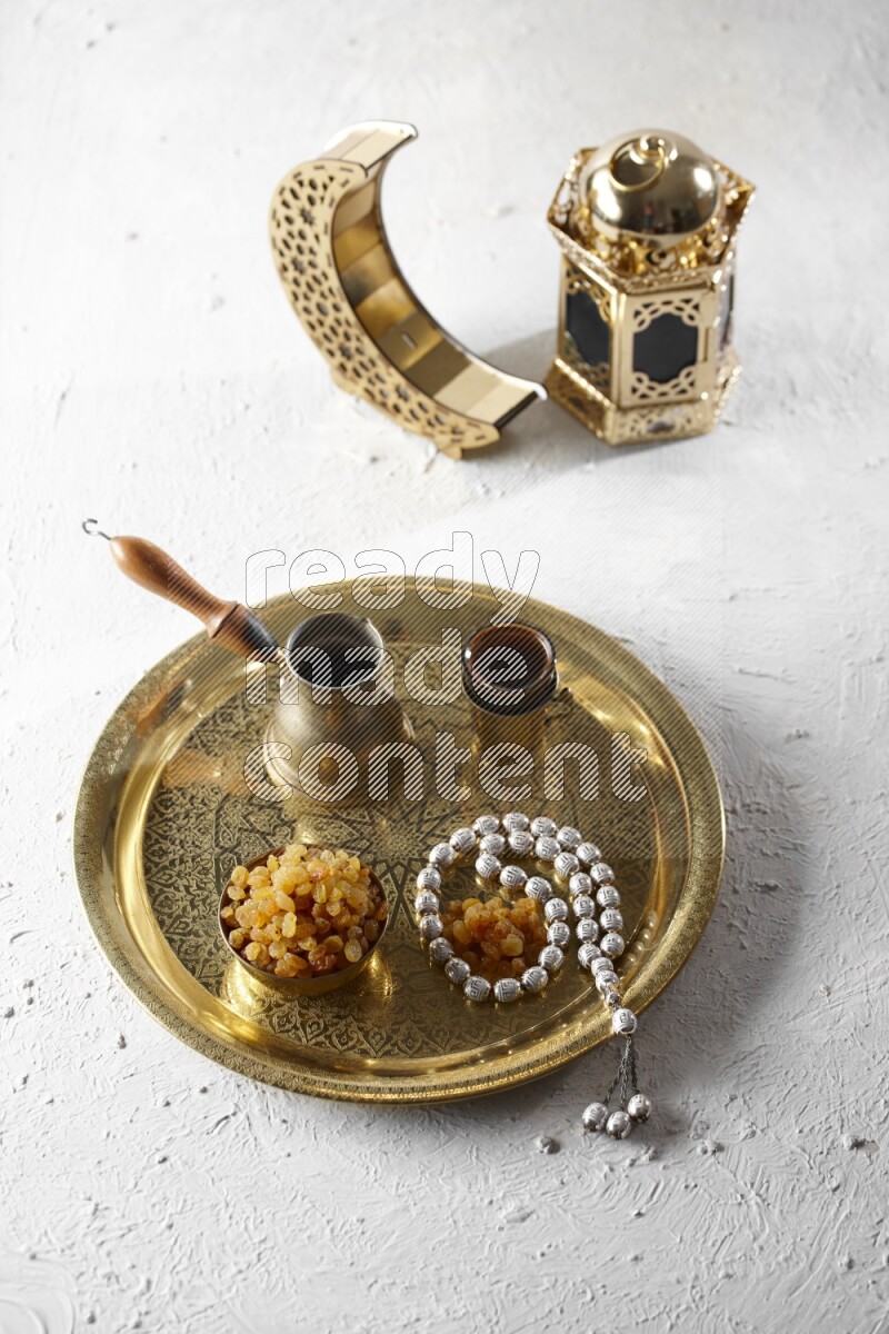 Raisins in a metal bowl with coffee and prayer beads on a tray beside lanterns in a light setup