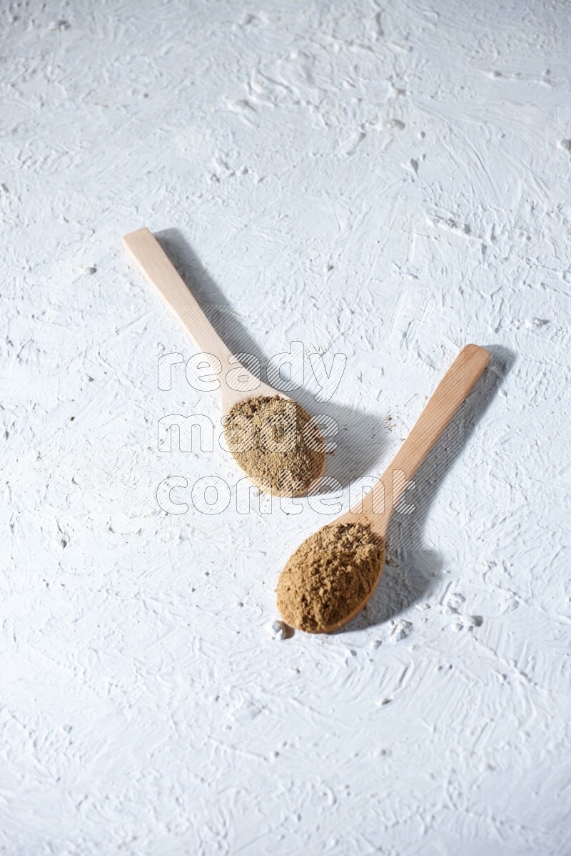 Wooden spoons full of allspice powder and allspice whole balls spreaded on a textured white flooring