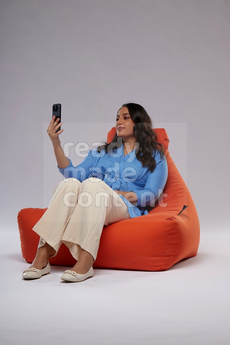 A woman sitting on an orange beanbag and taking selfie