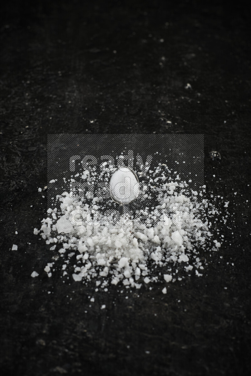 2 metal spoons filled with white salt on black background