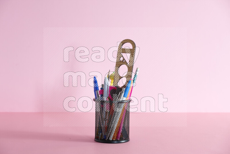 Pens, pencils and other different school supplies in a metal pen holder on rose background