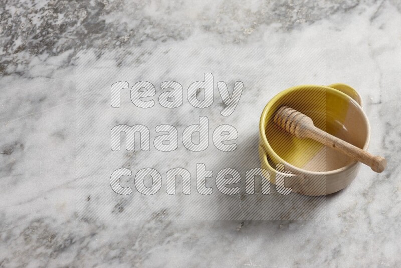 Multicolored pottery bowl with wooden honey dipper in it on grey marble background