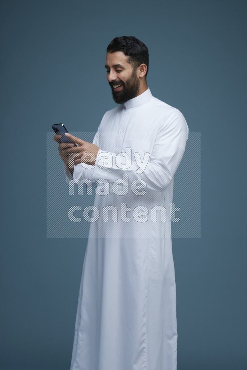 A man Texting in a blue background wearing Saudi Thob